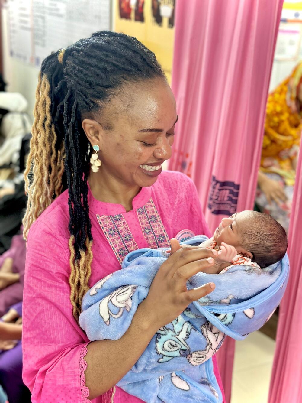 Die Hebamme Kindness Ngoh hält ein Neugeborenes im Arm, während sie sich um Mutter und Kind kümmert. © UNFPA